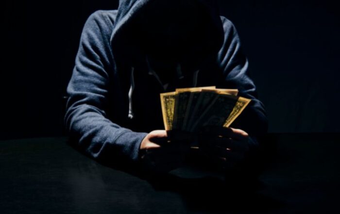 Hooded man holding money - a scammer