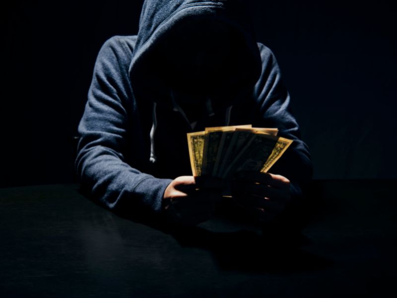 Hooded man holding money - a scammer