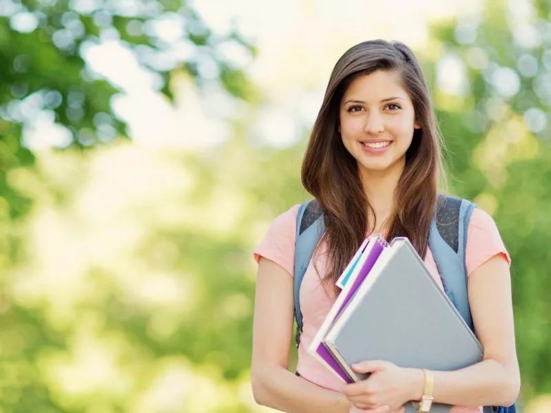 College woman holding books with a backpack on